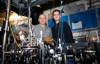 Two men standing behind an intricate display of wires and electronics