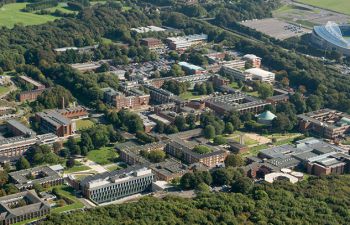 An aerial shot of the University of Sussex campus with a number of red-brick buildings surrounded by greenery