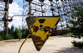 A faded and damaged yellow-and-black nuclear warning sign in the foreground on a disused nuclear plant site