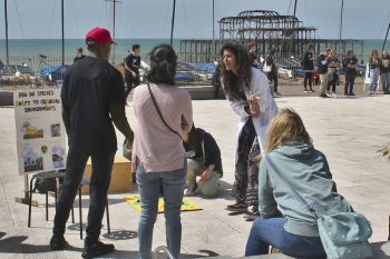 A scientist in a white lab coat speaking to crowds in front of the West Pier on Brighton seafront