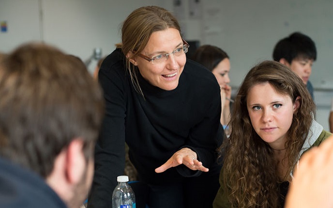 lecturer talking to students sitting round a table in a workshop