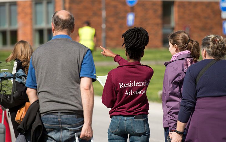 Image of student in residential advisor sweatshirt pointing at building with four other people